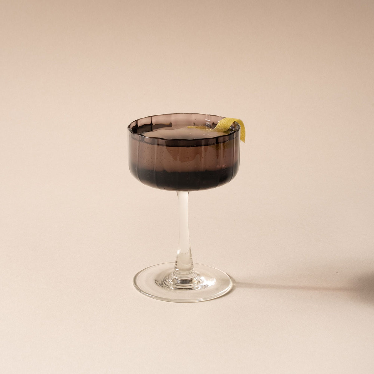 A cocktail in a coupe glass with a fluted bowl that is a grey purple color with a clear stem