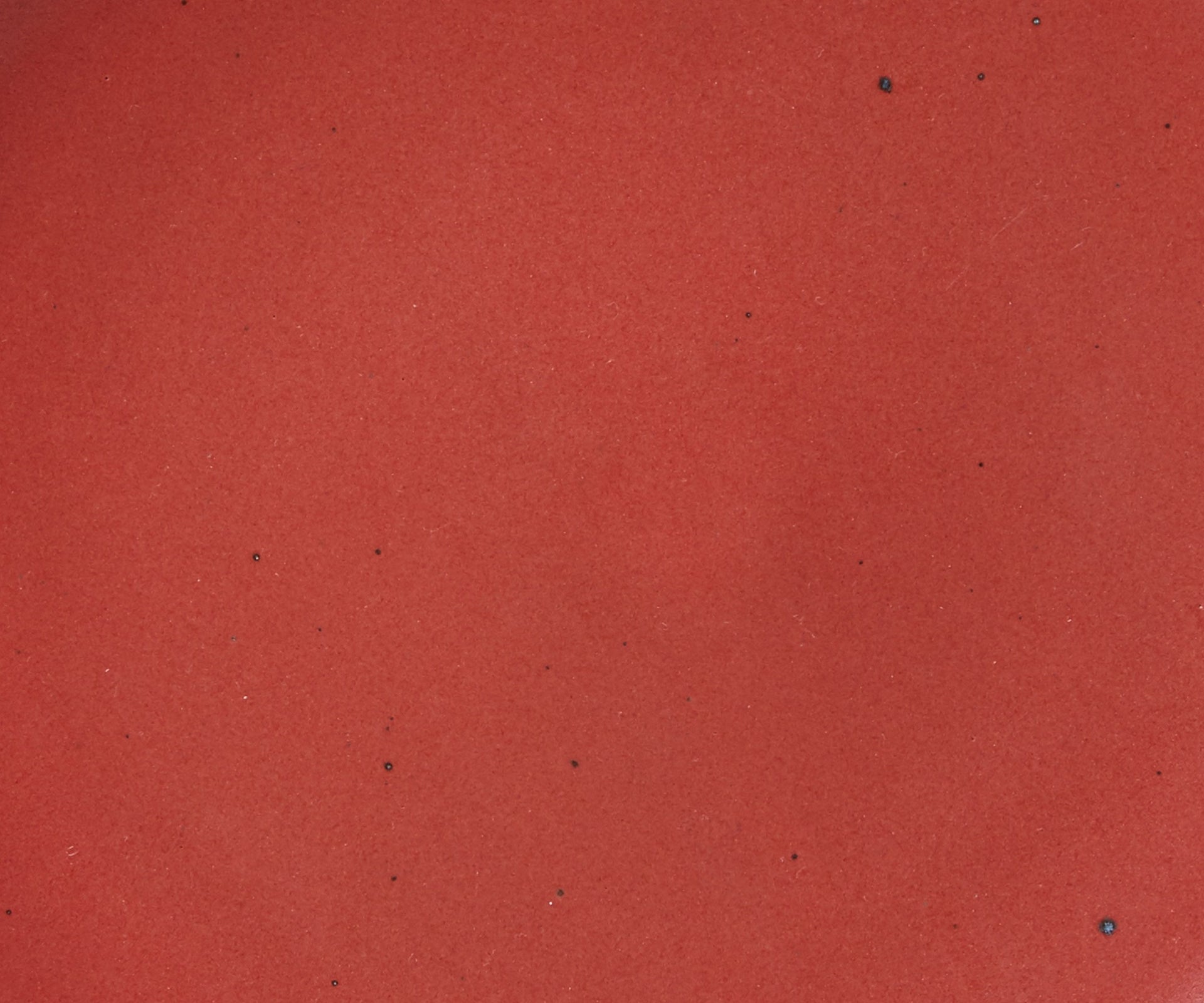 A closeup of a ceramic plate in a deep red color with iron speckles throughout