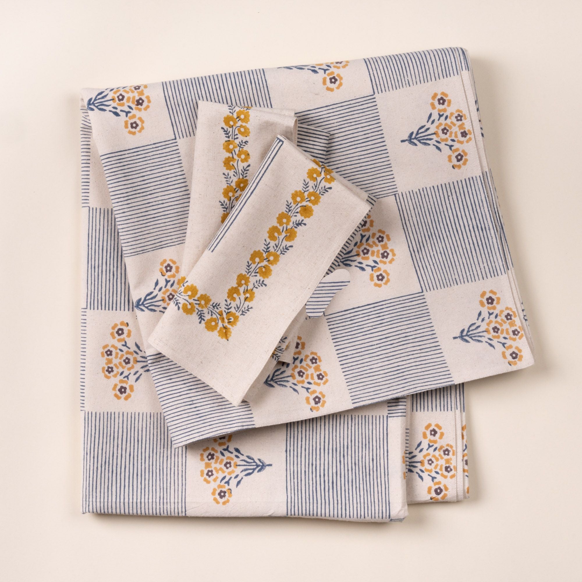 Folded blue-and-white checkered cloth tablecloth printed with small yellow flower bouquets, with similar napkins, on a light background