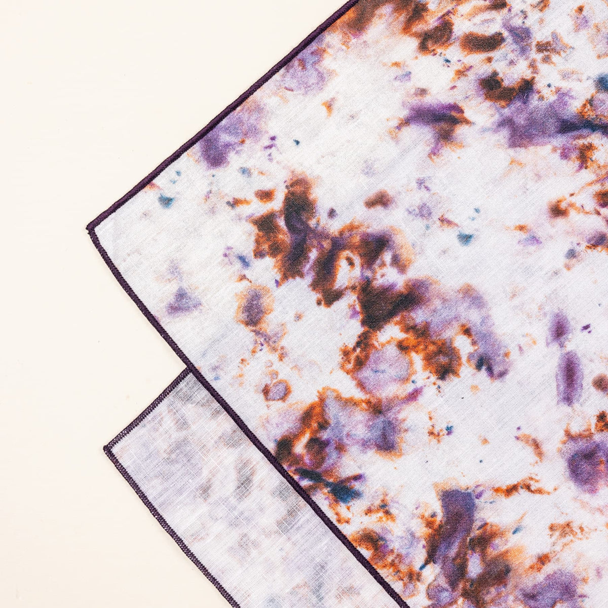 A close up of a corner of a table runner with a marble pattern featuring pink, purple, orange and white colors folded artfully