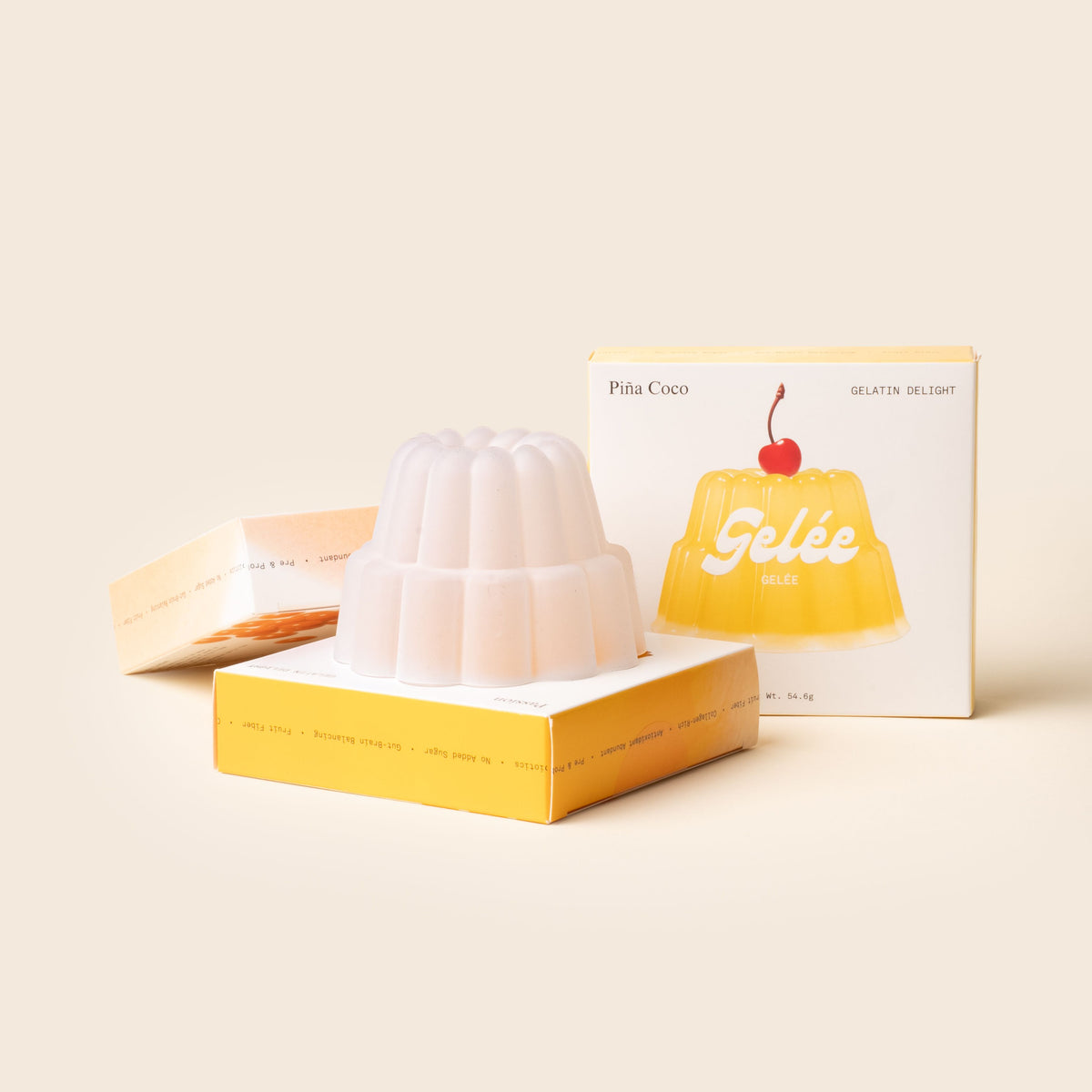 A white gelatin dessert mould sits atop its yellow Piña Coco “Gelée” box, with matching packaging and a cherry-topped illustration behind it.