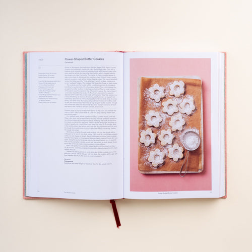 Open cookbook showing recipe text for flower-shaped butter cookies with photo of cookies dusted with powdered sugar.