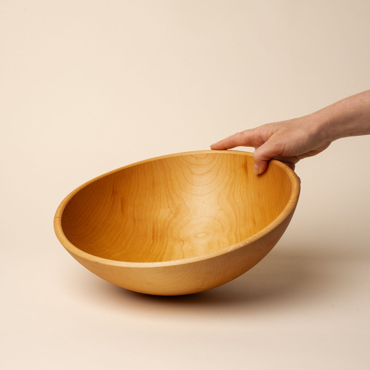A hand holds out a large maple wood bowl