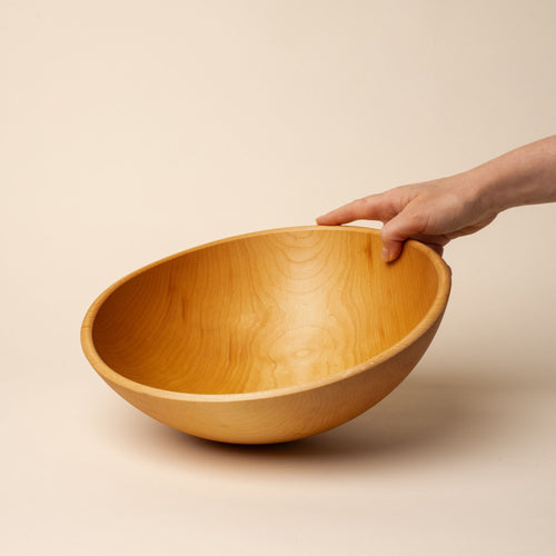 A hand holds out a large maple wood bowl