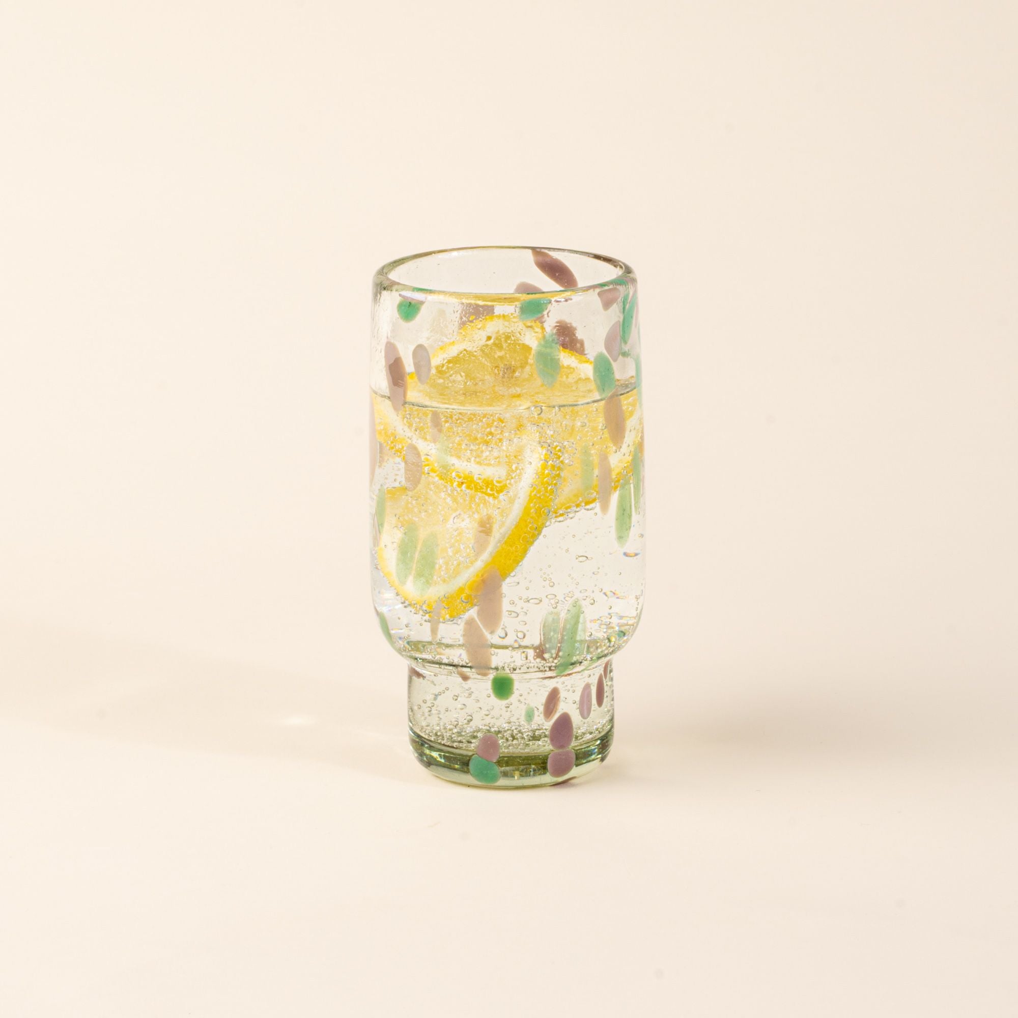 A tall clear glass with pastel green and pink speckled patterns, filled with water and lemon slices.