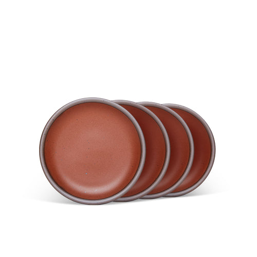 4 dessert sized ceramic plates in a cool burnt terracotta color featuring iron speckles and an unglazed rim.