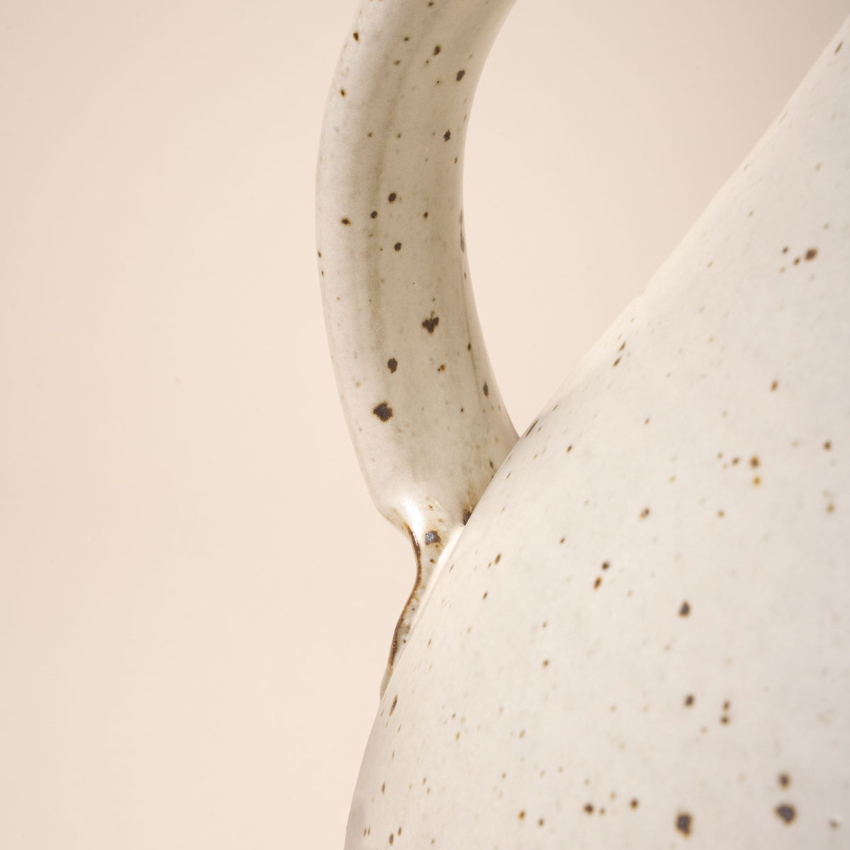 A closeup of the bottom of the handle connected to the body of a ceramic pitcher.