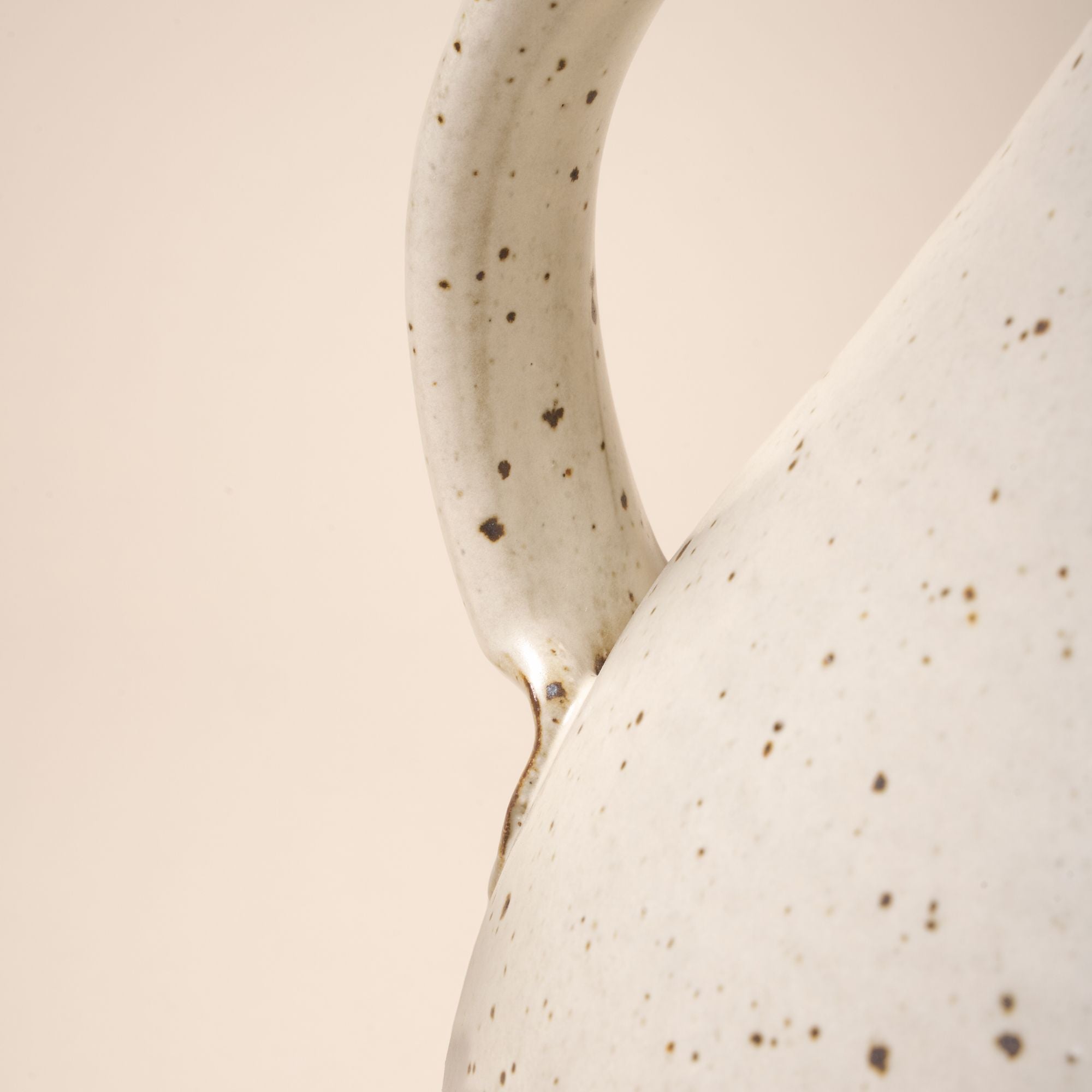 A closeup of the bottom of the handle connected to the body of a ceramic pitcher.