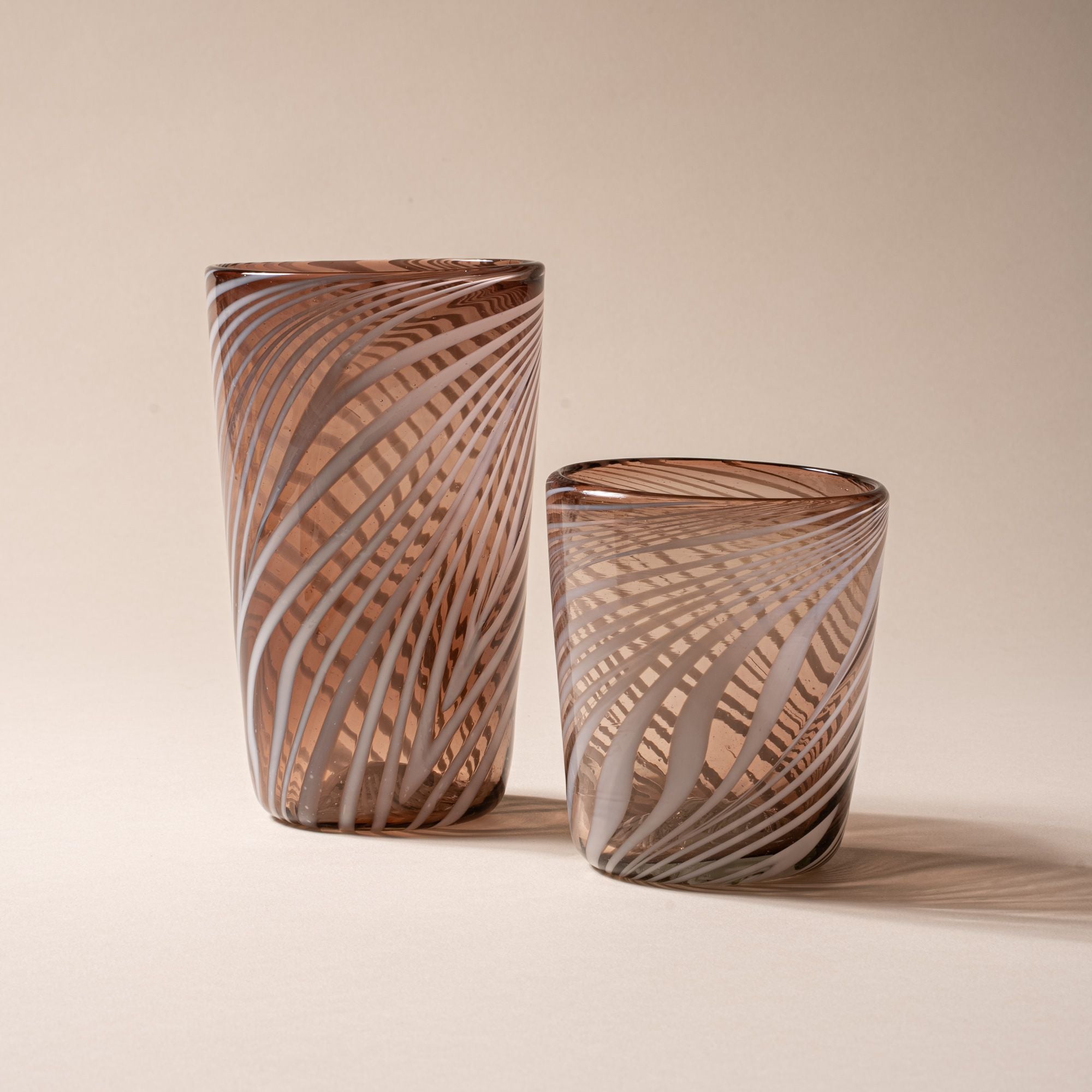 Smoky brown glass tumbler and pint glass with white diagonal swirl pattern on a neutral background.