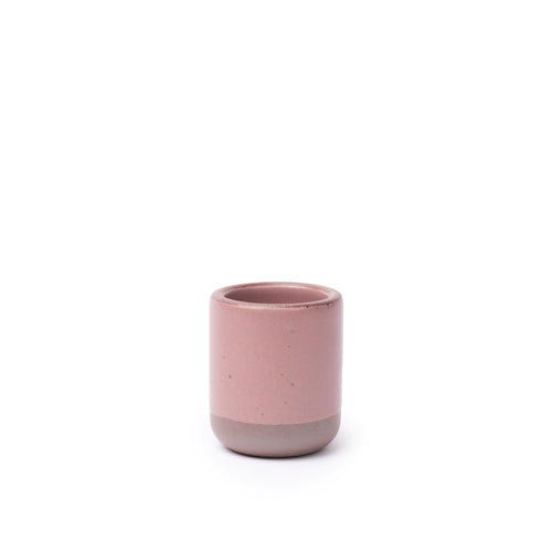 A small, short ceramic mug cup in a dusty mauve pink color featuring iron speckles and unglazed rim and bottom base.