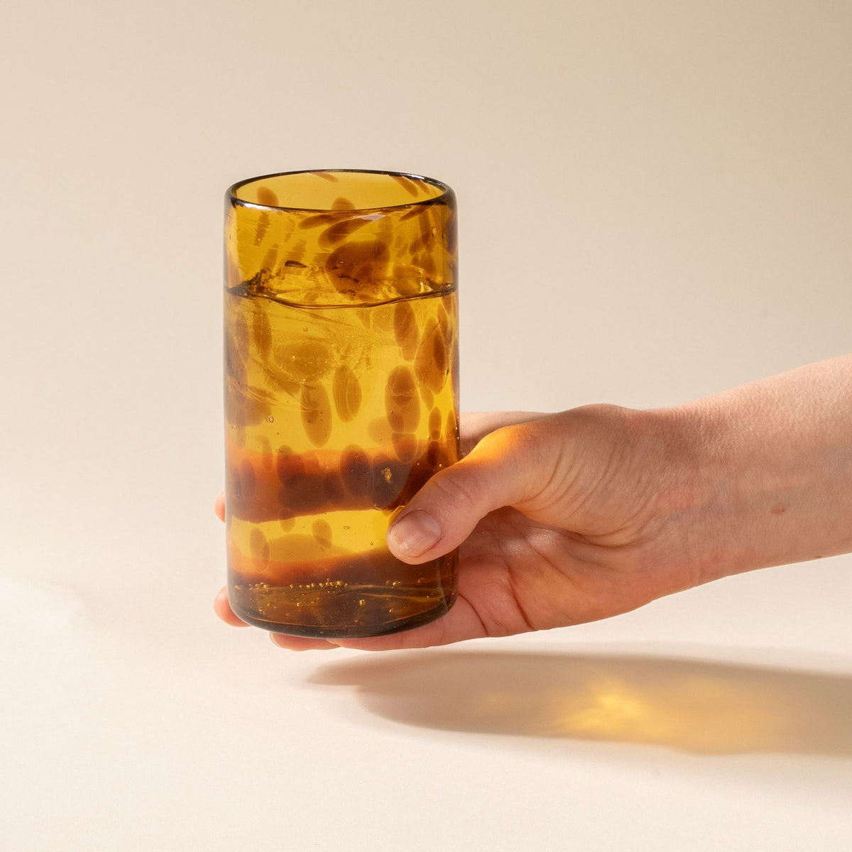 A hand holds a tortoiseshell tall transparent drinking glass, filled with ice water