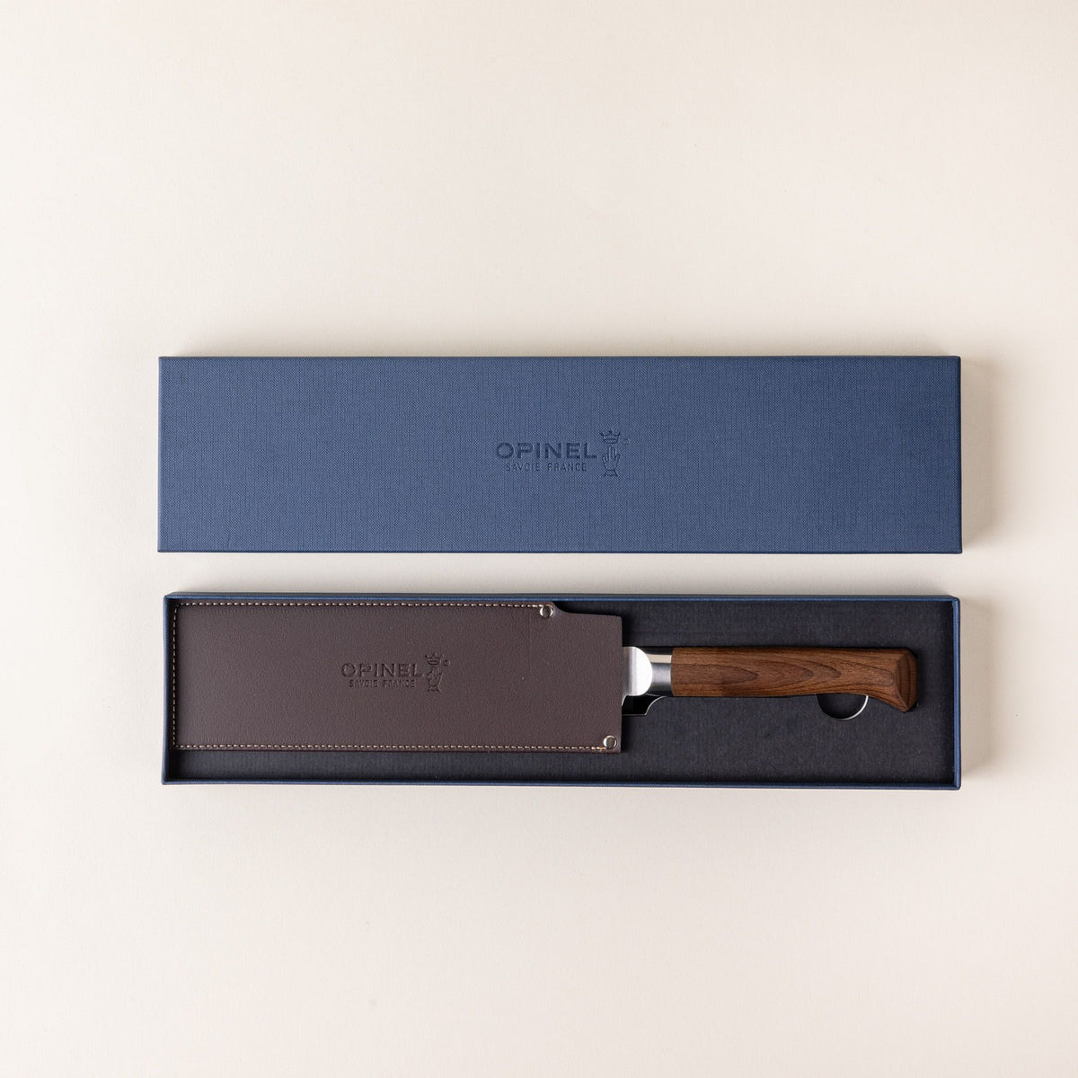 A santoku knife with a sharp steel blade with dimples and a beveled dark wood handle sits in a packaging box with a leather sleeve on the blade.