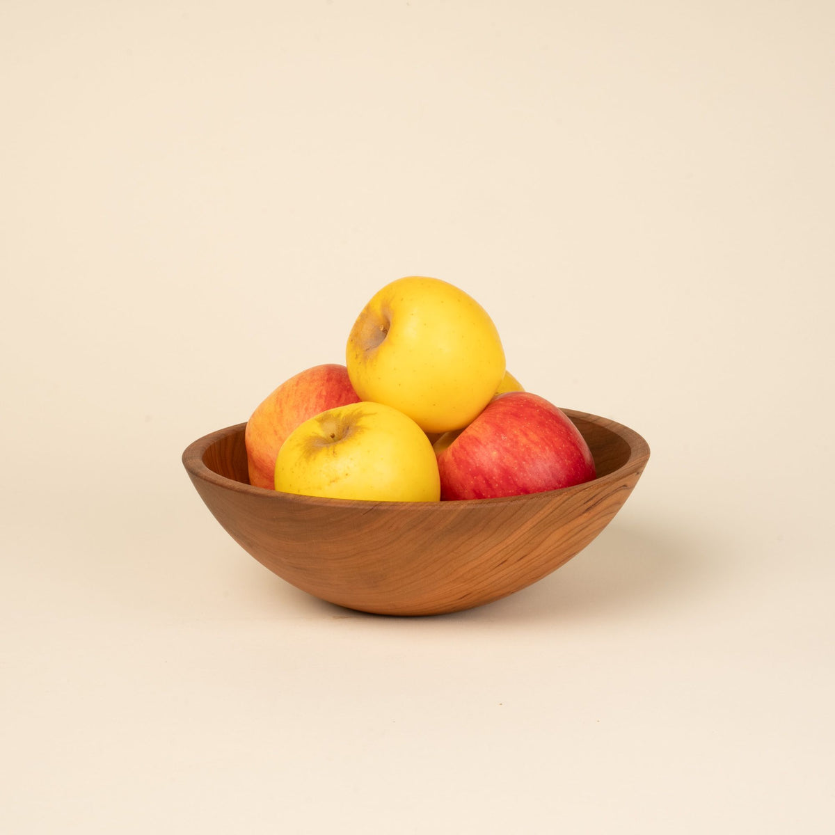 A pile of apples in a medium sized round cherry wood bowl