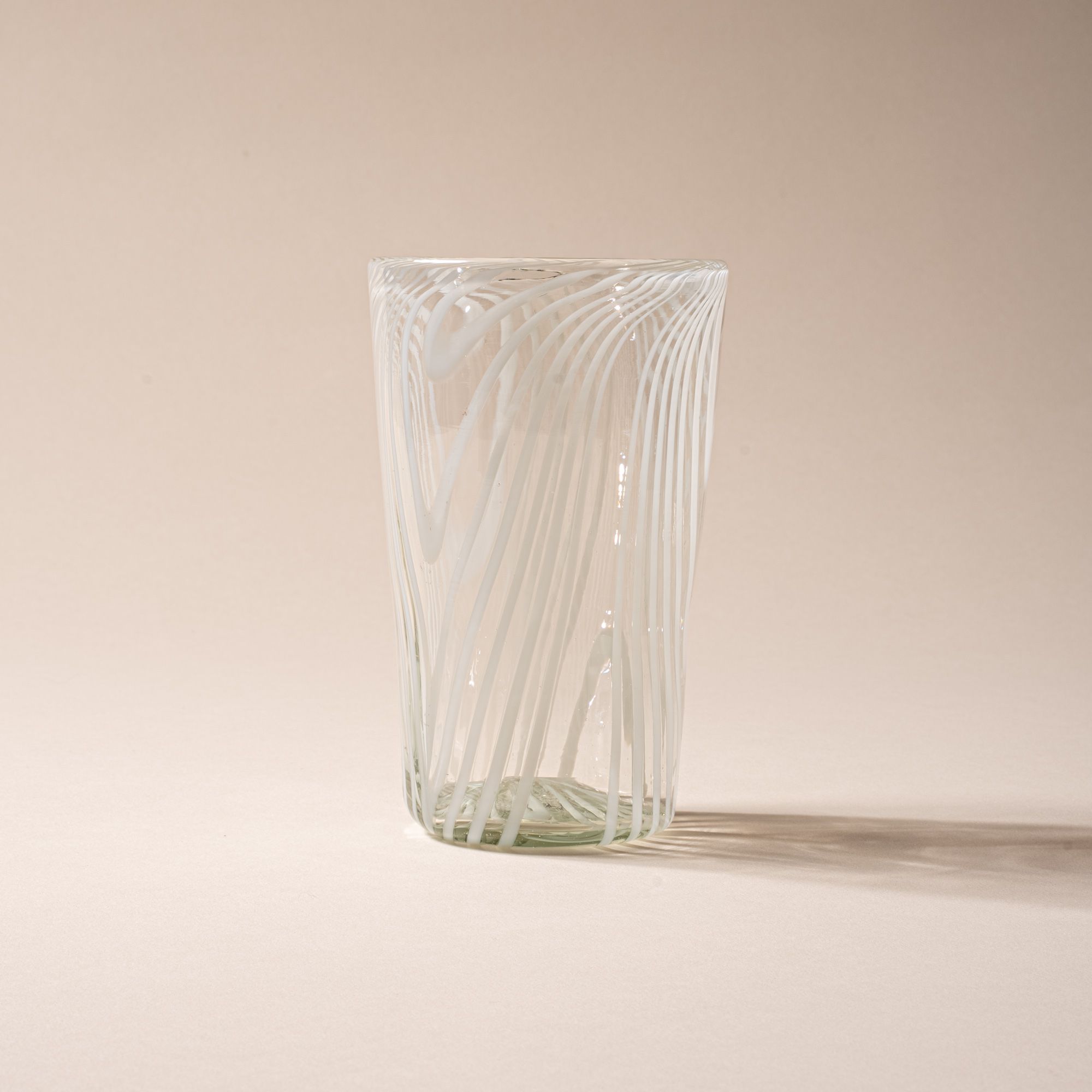 Clear pint glass with white diagonal swirl pattern against a neutral background.
