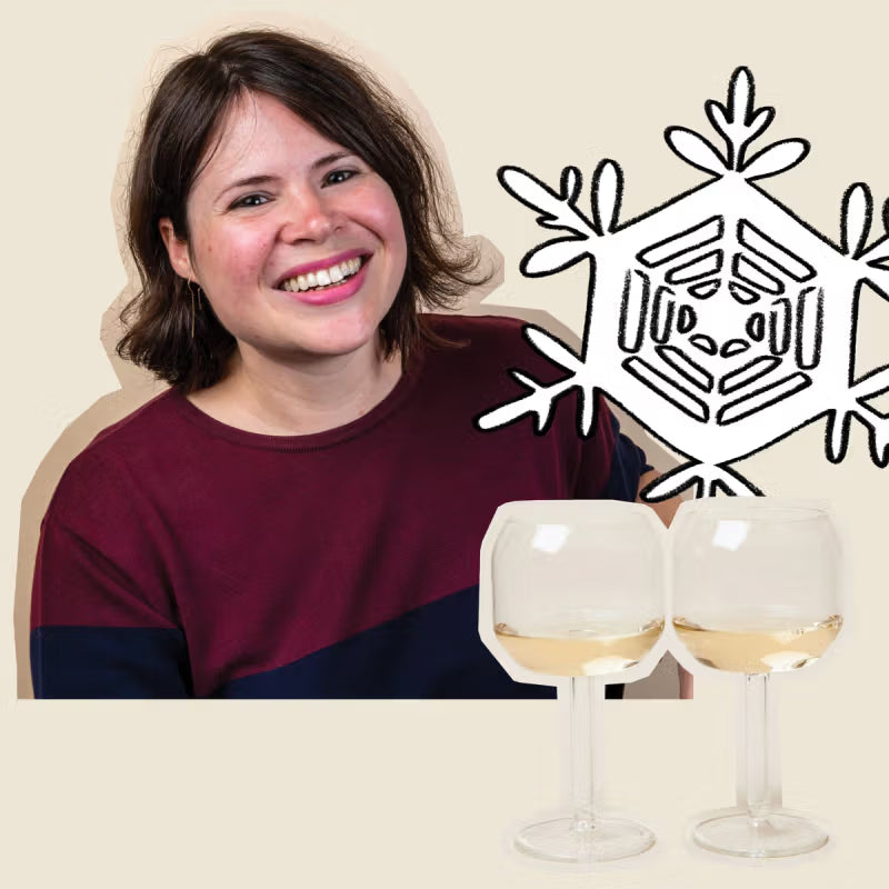Smiling person with short hair wearing a burgundy top is next to a line drawing of a snowflake. Two wine glasses with white wine are in the foreground.