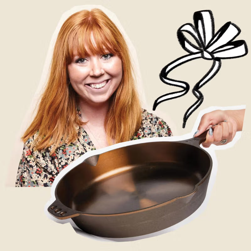 A cast iron skillet held by a hand in the foreground, alongside a smiling person with red hair. A black and white bow illustration is in the background, all against a light beige backdrop.
