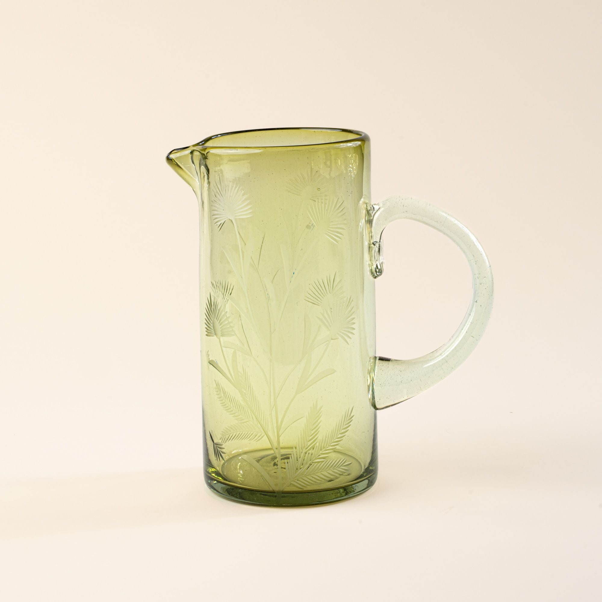 A large glass olive pitcher with handle made of recycled glass with etched thistle designs on it.
