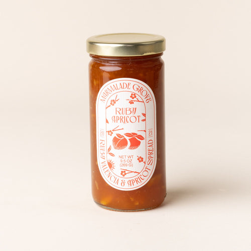 A jar of Marmalade Grove Ruby Apricot Spread, featuring a red and white label with fruit and floral illustrations.