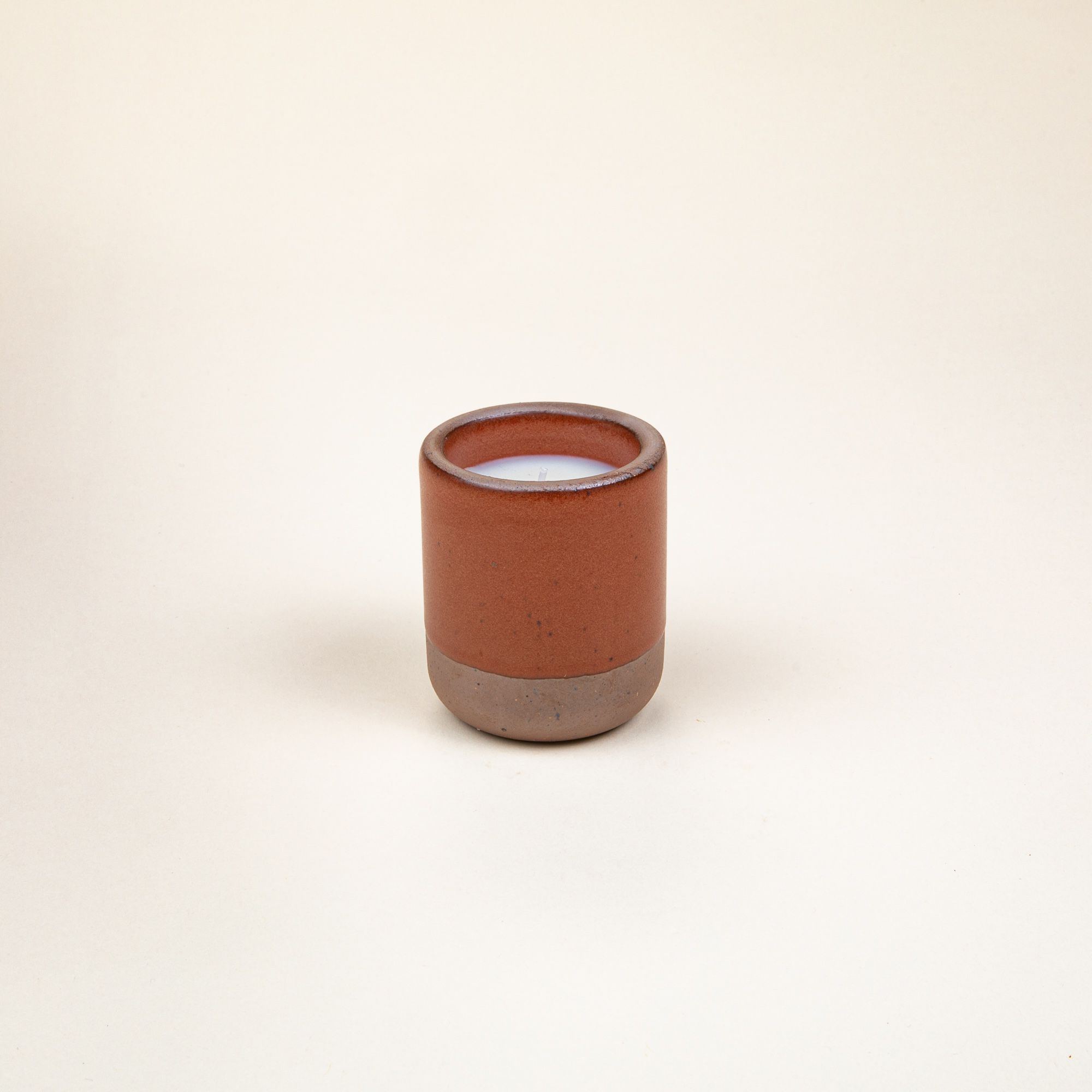 Small ceramic vessel in a cool terracotta color with candle inside.