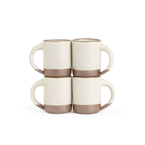 Four medium sized ceramic mugs with handles in a warm, tan-toned, off-white color featuring iron speckles and unglazed rim and bottom base, stacked in sets of 2.