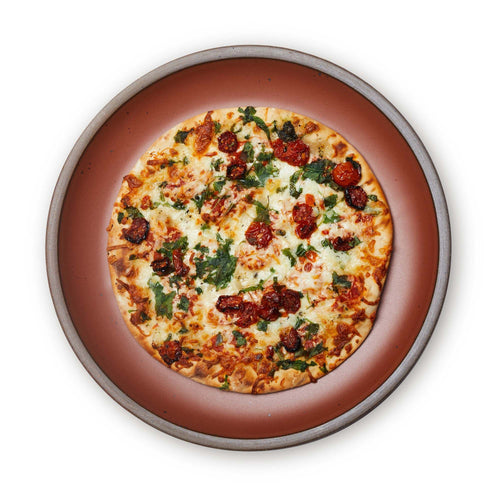 A pizza on a large ceramic platter in a cool burnt terracotta color featuring iron speckles and an unglazed rim.