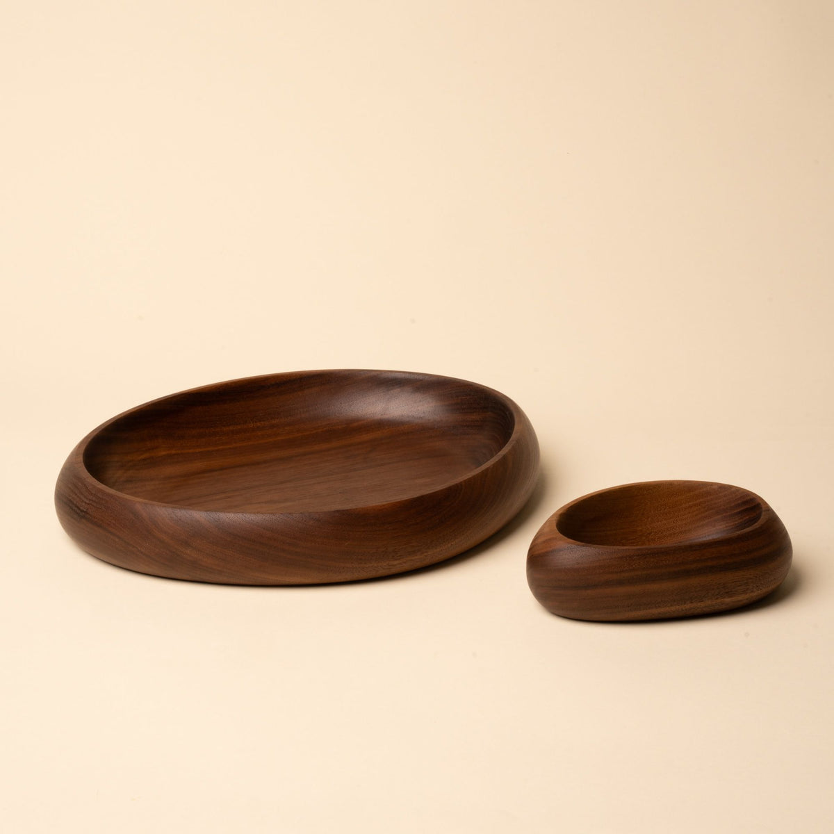 Two carved walnut bowls in different sizes, one wide and shallow, the other smaller and deeper, shown on a neutral background.
