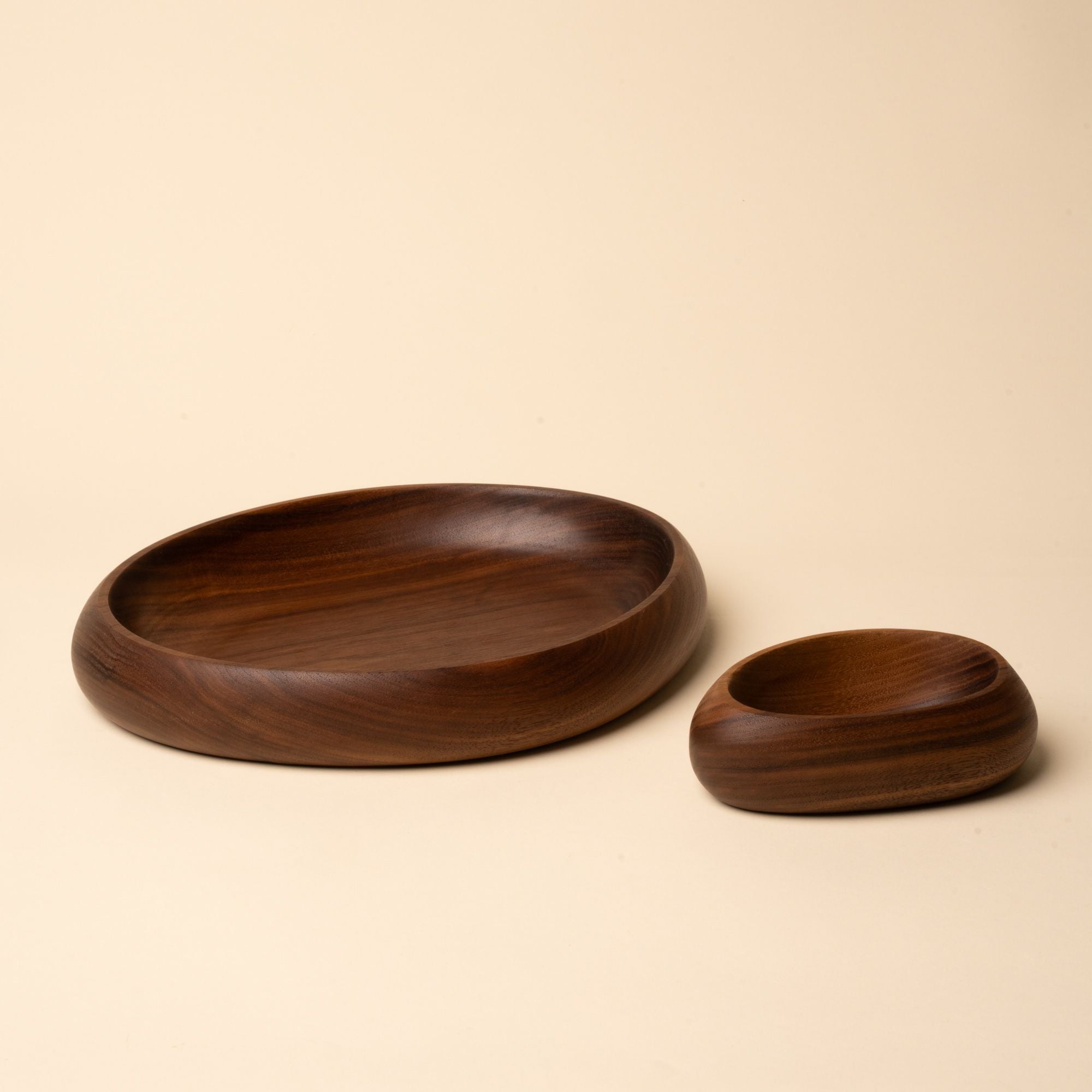 Two carved walnut bowls in different sizes, one wide and shallow, the other smaller and deeper, shown on a neutral background.