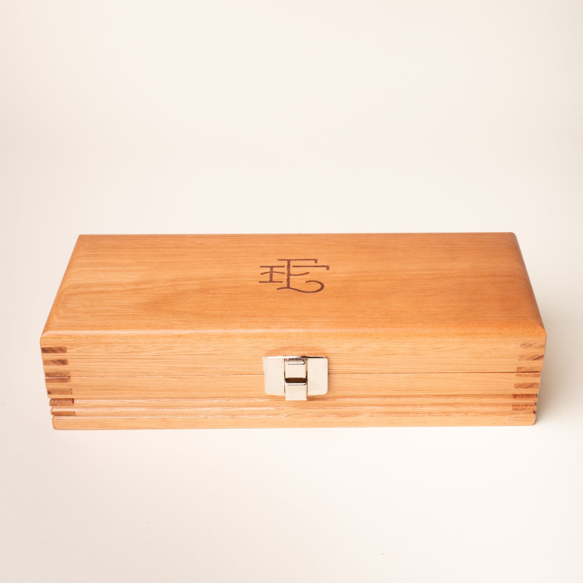 Closed wooden knife box with metal clasp and engraved logo on the lid, set against a neutral background.