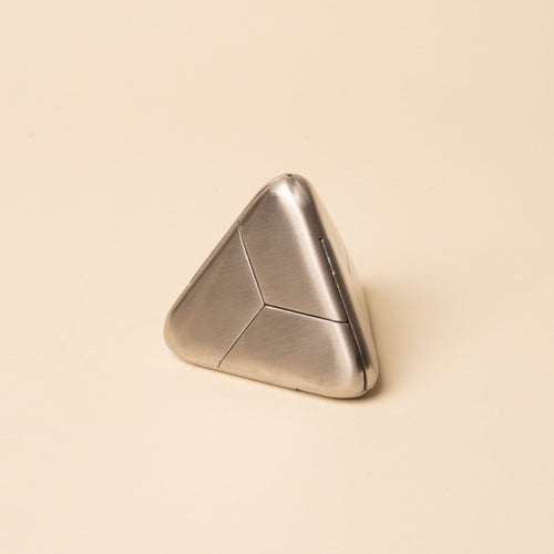 Triangular silver metal puzzle with smooth rounded edges and subtle seam lines, resting on a beige background.