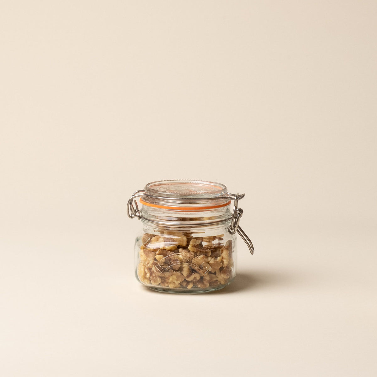 A shorter storage glass square jar, filled with nuts, topped with a lid with a rubber seal and steel clip closure.