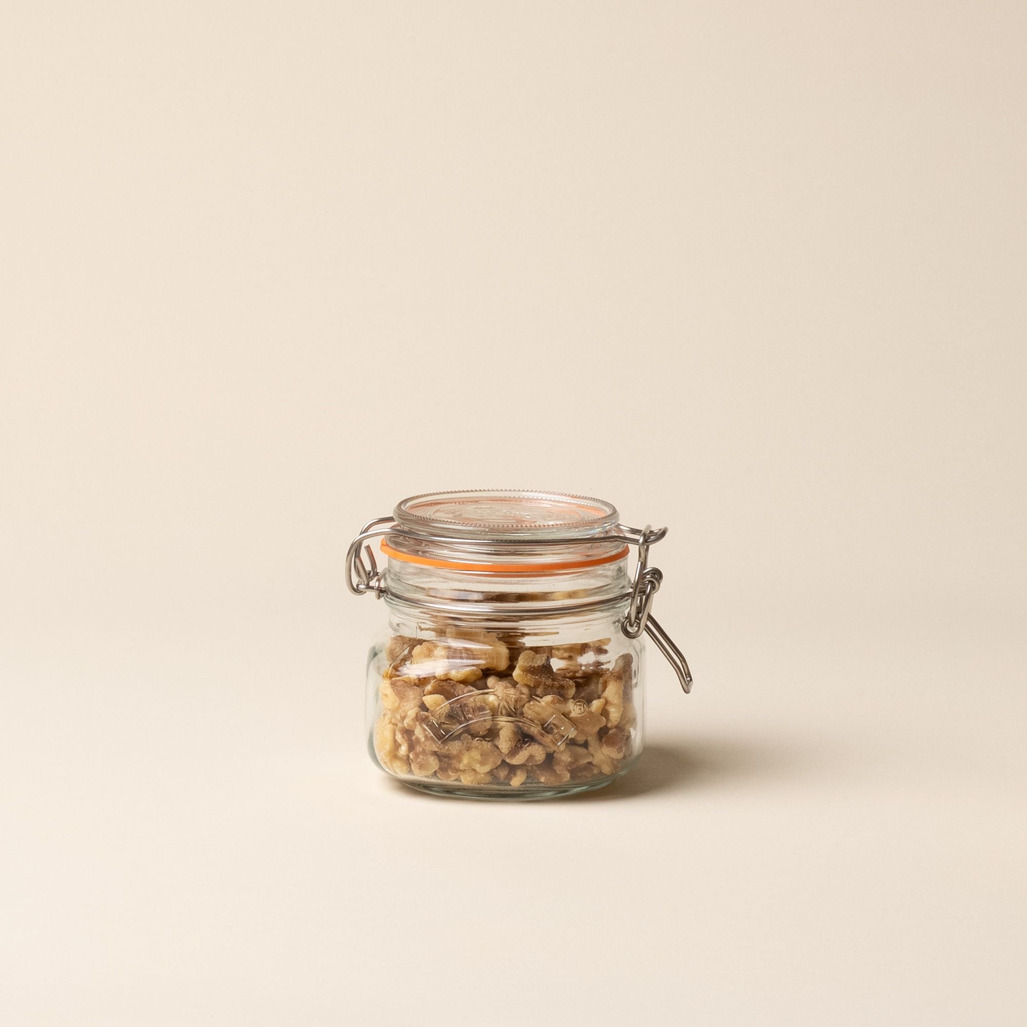 A shorter storage glass square jar, filled with nuts, topped with a lid with a rubber seal and steel clip closure.