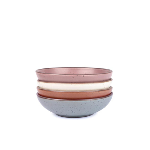 A stack of 4 dinner-sized shallow ceramic bowls in a warm off-white, cool terracotta, blue-grey and dusty mauve pink colors featuring iron speckles and an unglazed rim