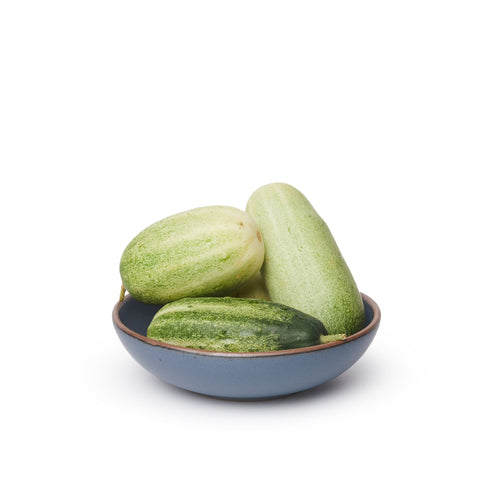 A dinner-sized shallow ceramic bowl in a cool, medium blue color featuring iron speckles and an unglazed rim, filled with cucumbers