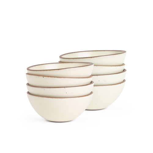 A stack of 8 medium rounded ceramic bowls in a warm off-white color featuring iron speckles and an unglazed rim