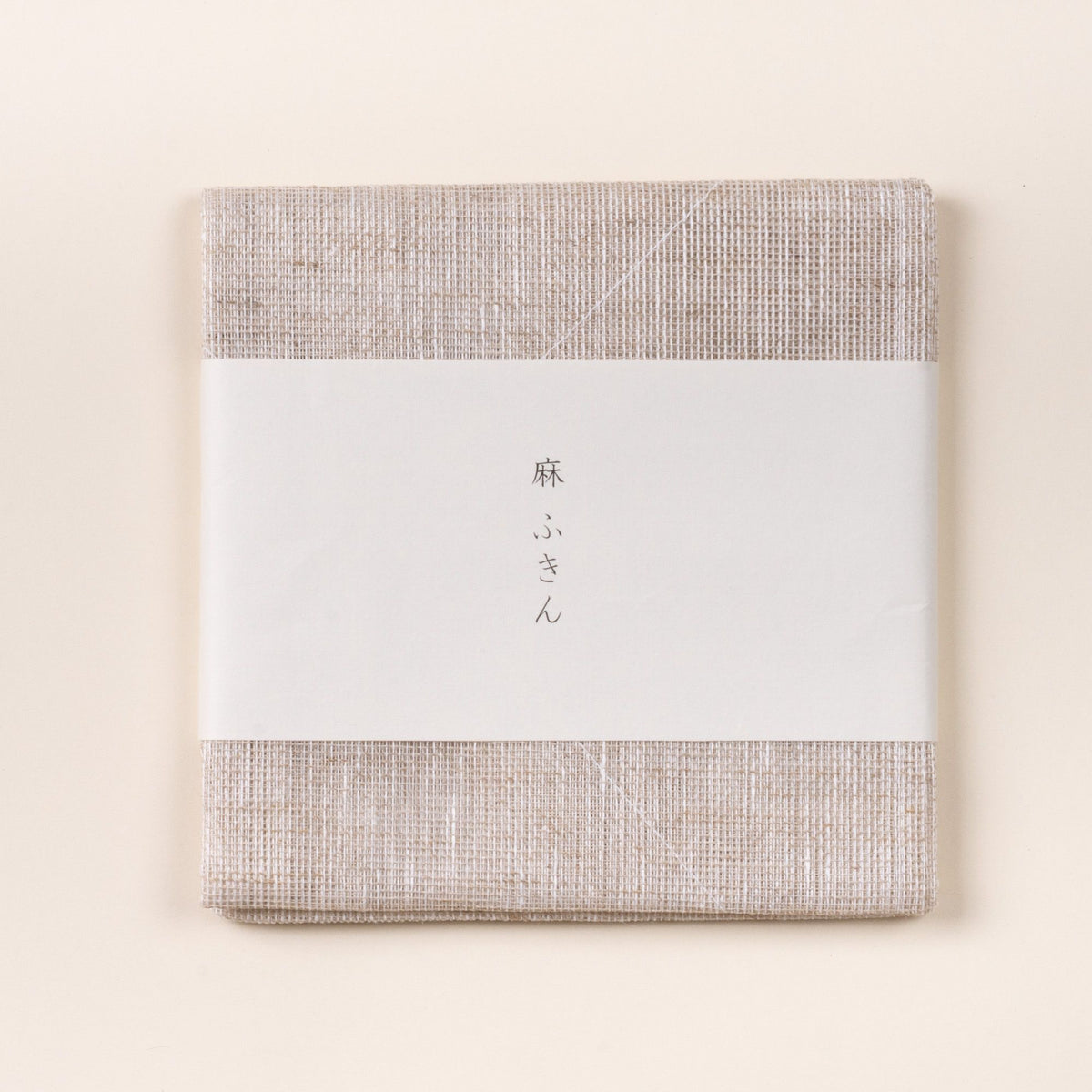 Folded natural linen cleaning cloth with a white paper band featuring Japanese text, photographed on a light background.