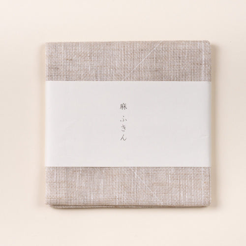 Folded natural linen cleaning cloth with a white paper band featuring Japanese text, photographed on a light background.