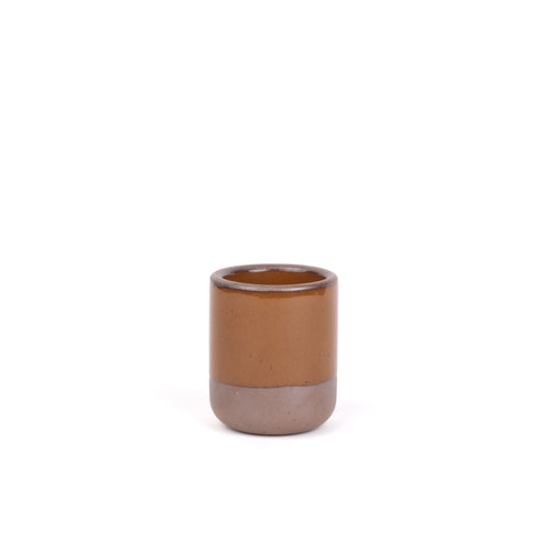 A small, short ceramic mug cup in a glossy caramel brown color featuring iron speckles and unglazed rim and bottom base.