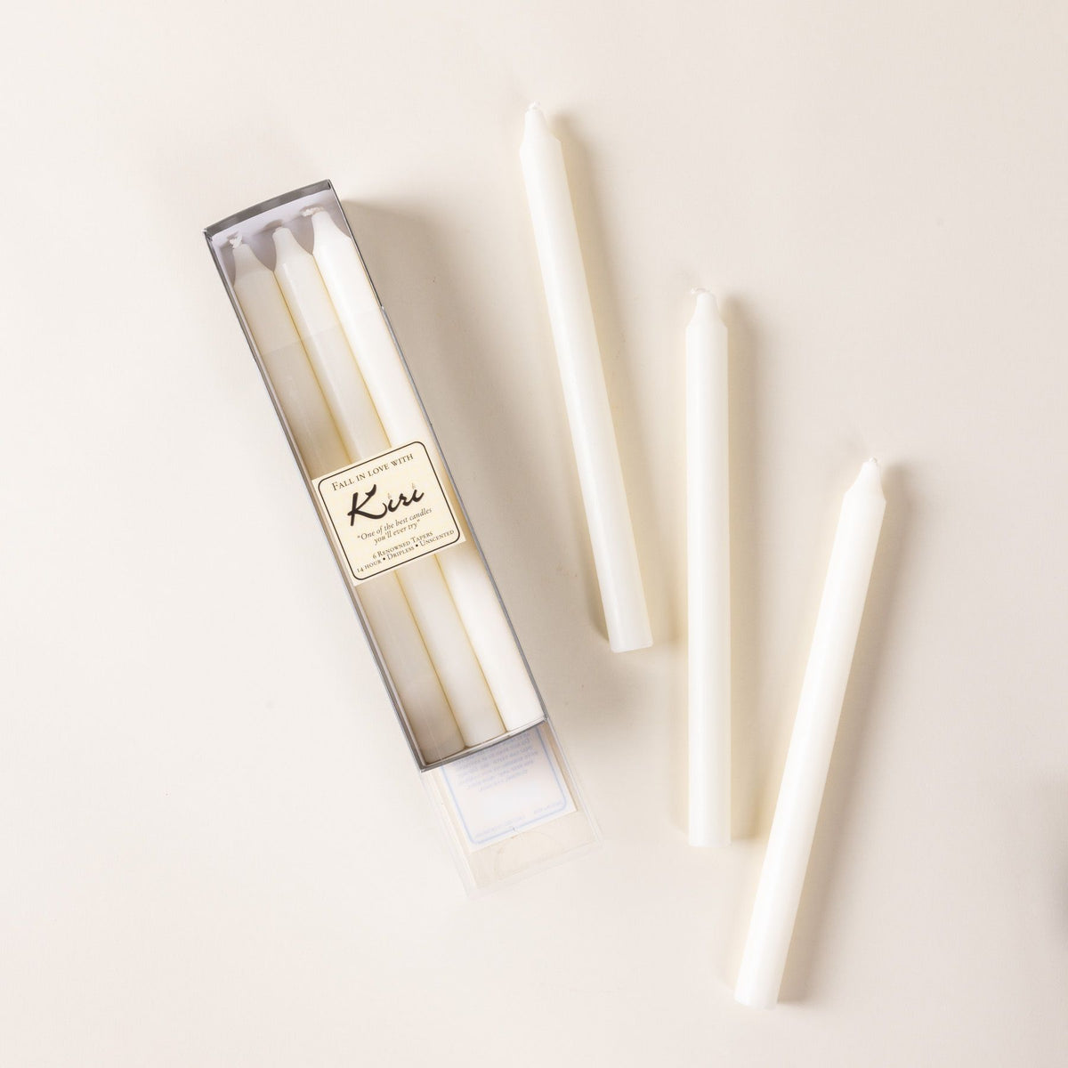 A narrow box of white taper candles, with 3 arranged outside of the box.