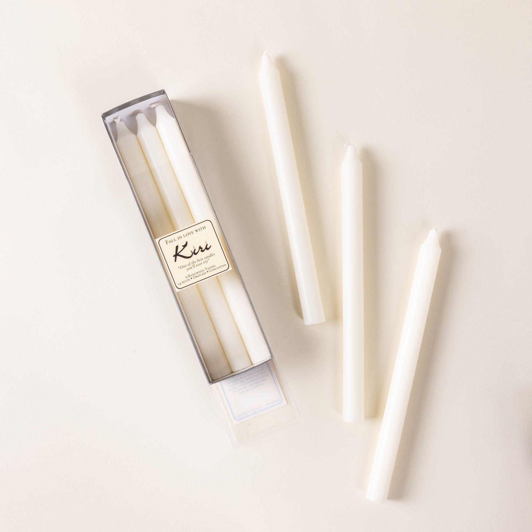 A narrow box of white taper candles, with 3 arranged outside of the box.