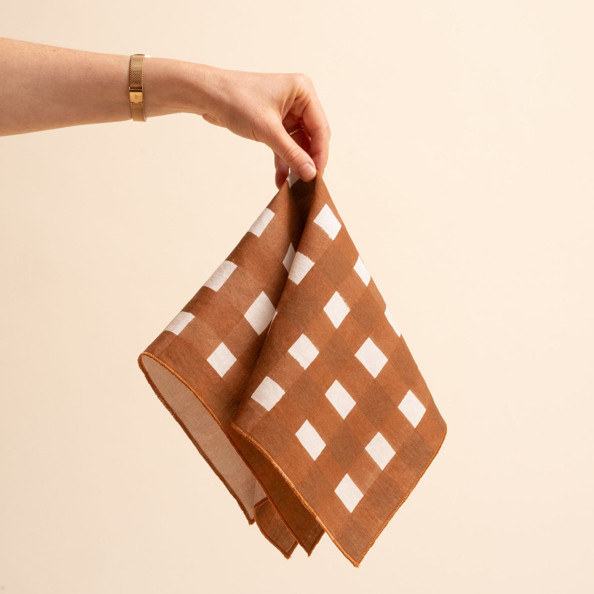 A hand holds out a square linen napkin with a brown and white crosshatch pattern
