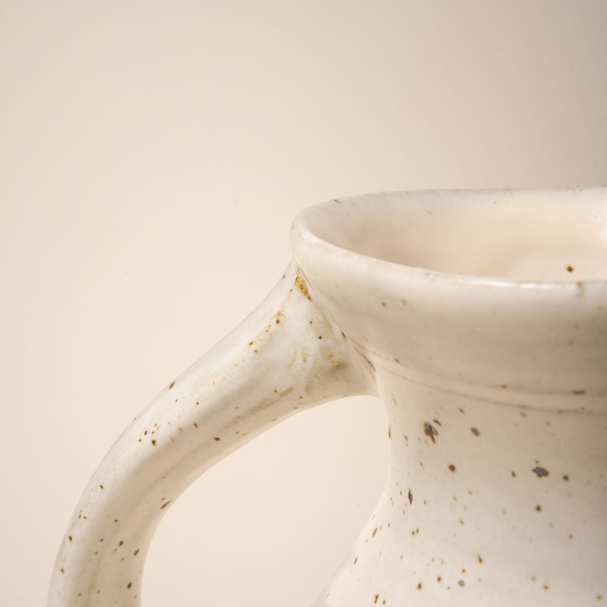 A closeup of the top of the handle connected to the top of a ceramic pitcher.