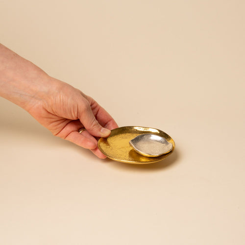 A hand holds out a small round gold dish with nesting chrome dish with a hammered texture