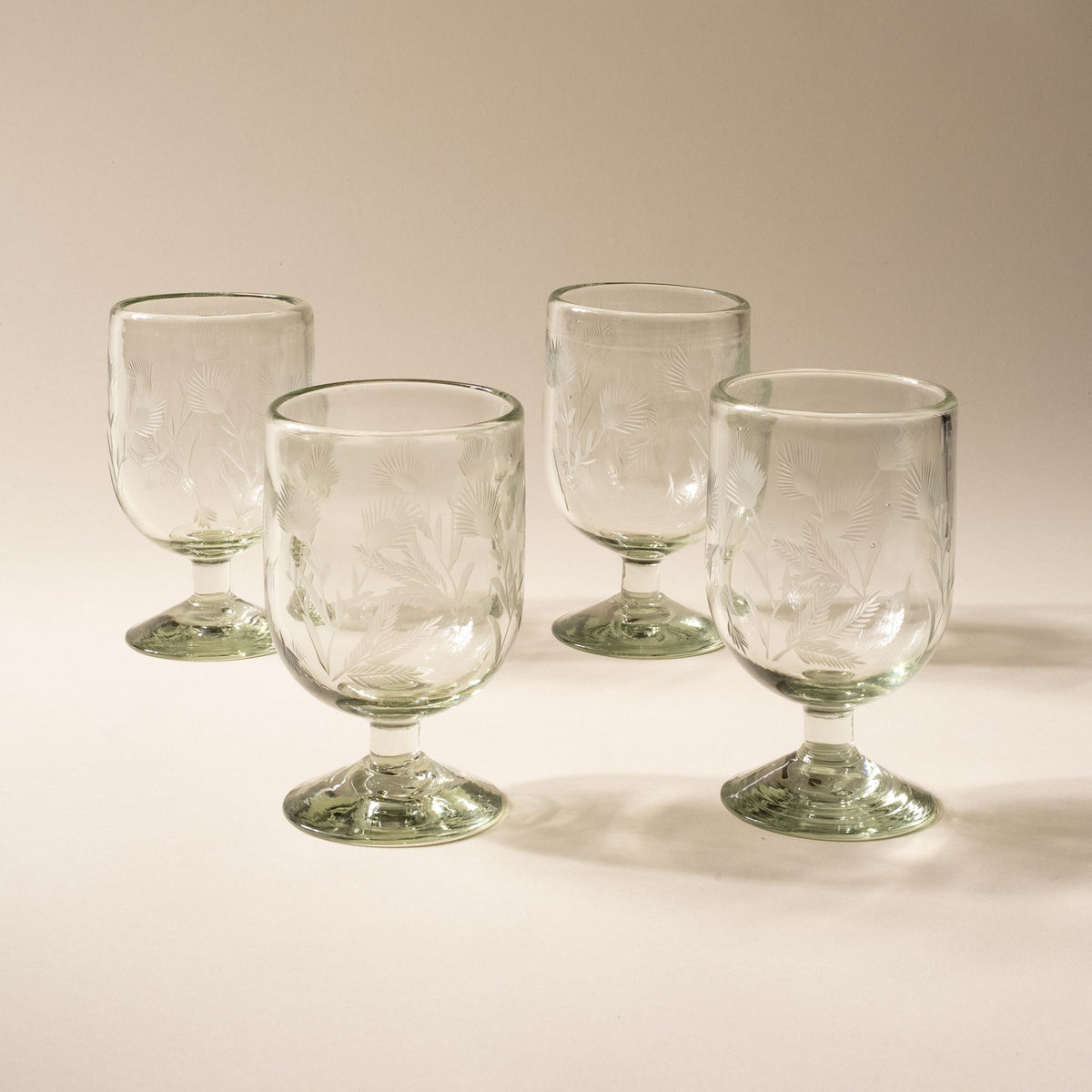A clear short wine glass made of recycled glass with etched thistle designs on it