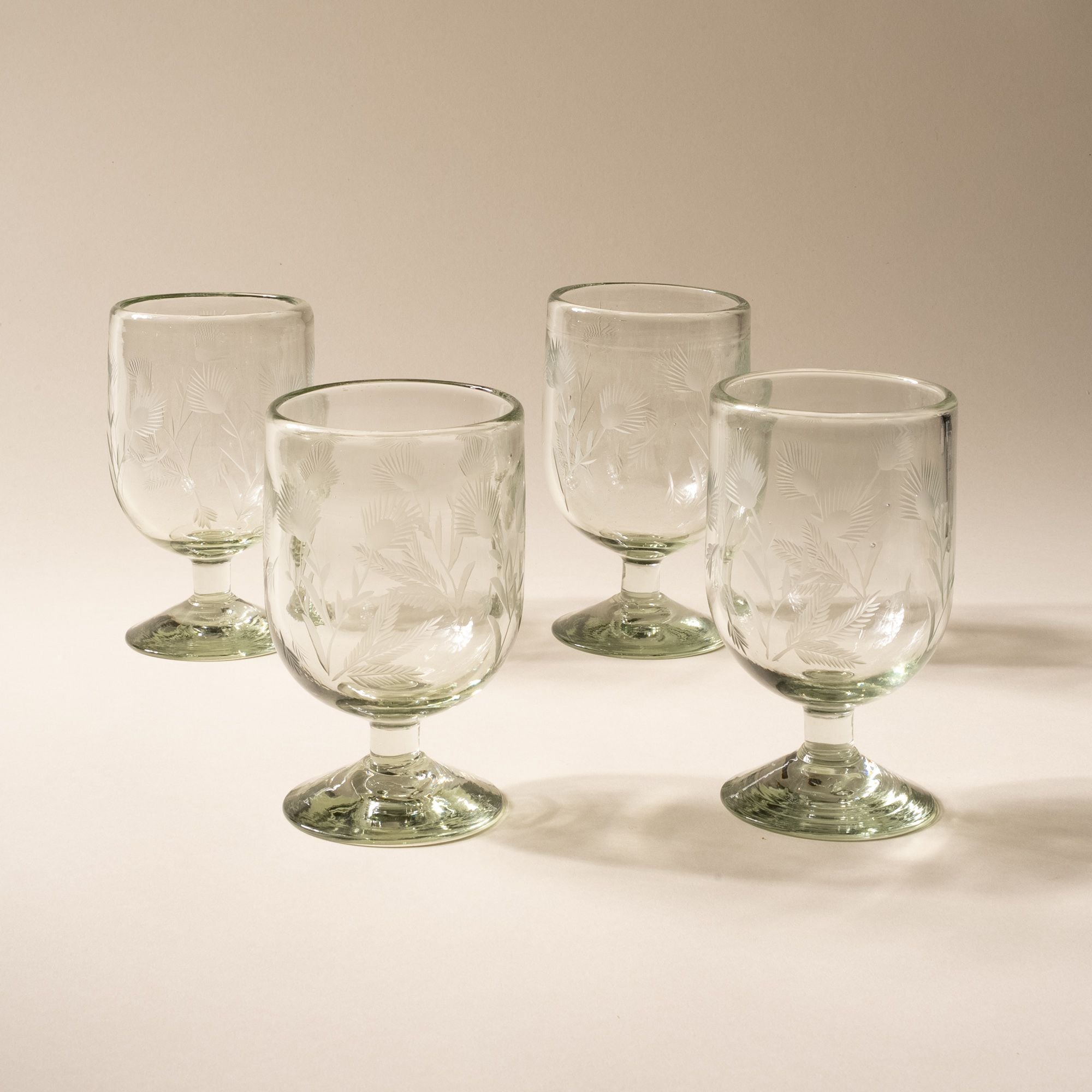 A clear short wine glass made of recycled glass with etched thistle designs on it