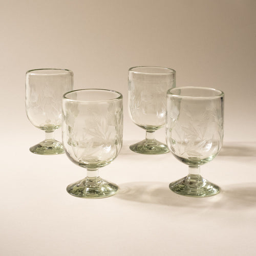 A clear short wine glass made of recycled glass with etched thistle designs on it