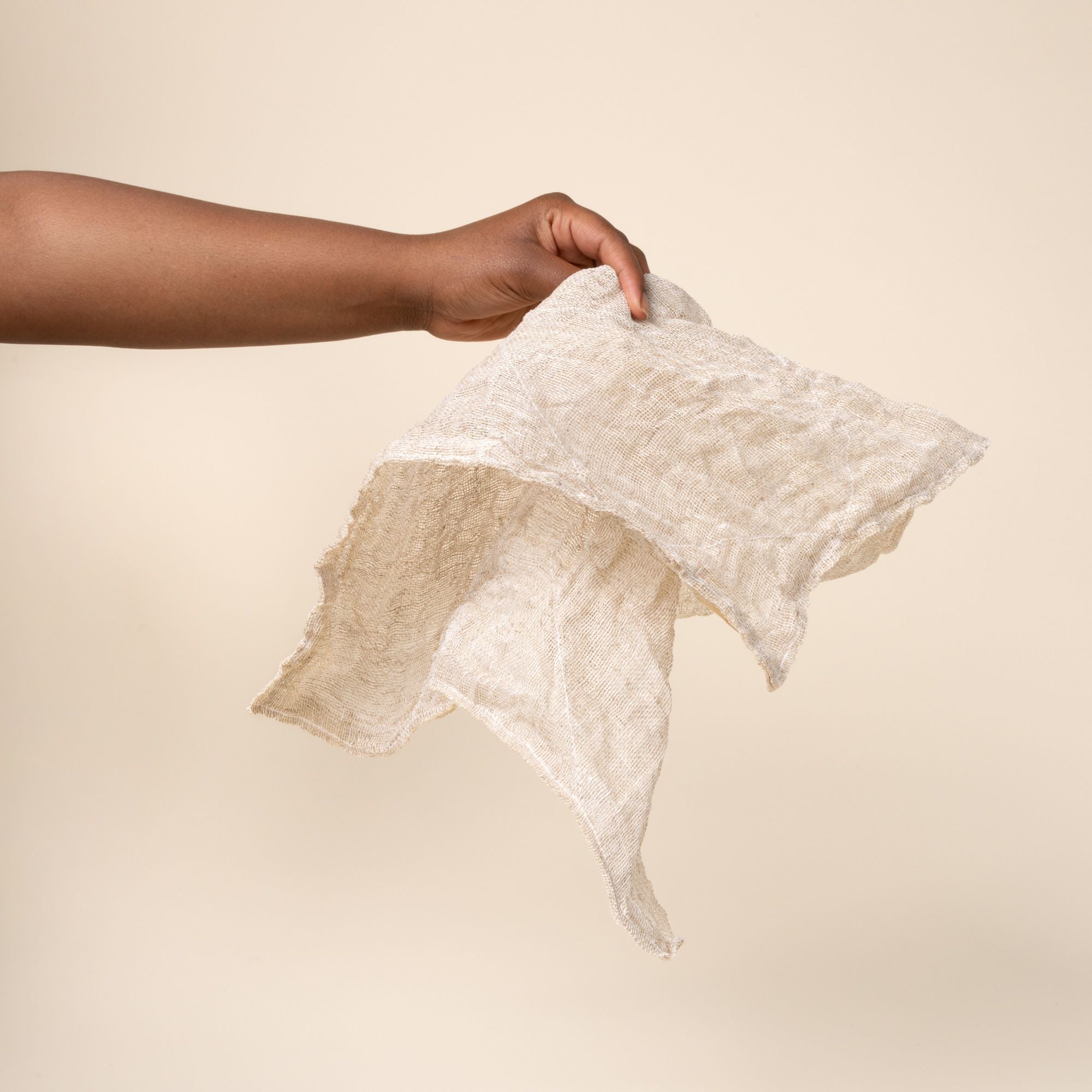 Hand holding a rigid and dry natural linen cleaning cloth showing a subtle woven texture and stitched edges.