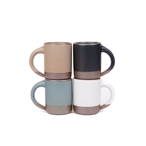 Four medium sized ceramic mugs with handles in a blue-grey, graphite black, cool white, and warm pale brown colors featuring iron speckles and unglazed rim