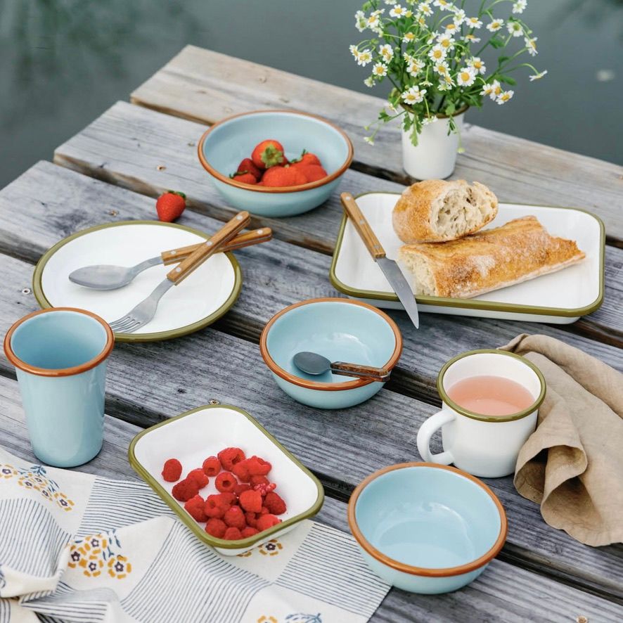 Outdoor enamelware picnic set up on a dock with white and robin egg's blue enamel dishes, bread, berries, and flowers.