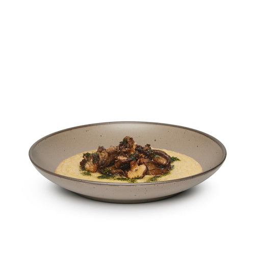 A dinner entrée in a large ceramic plate with a curved bowl edge in a warm pale brown color featuring iron speckles and an unglazed rim.