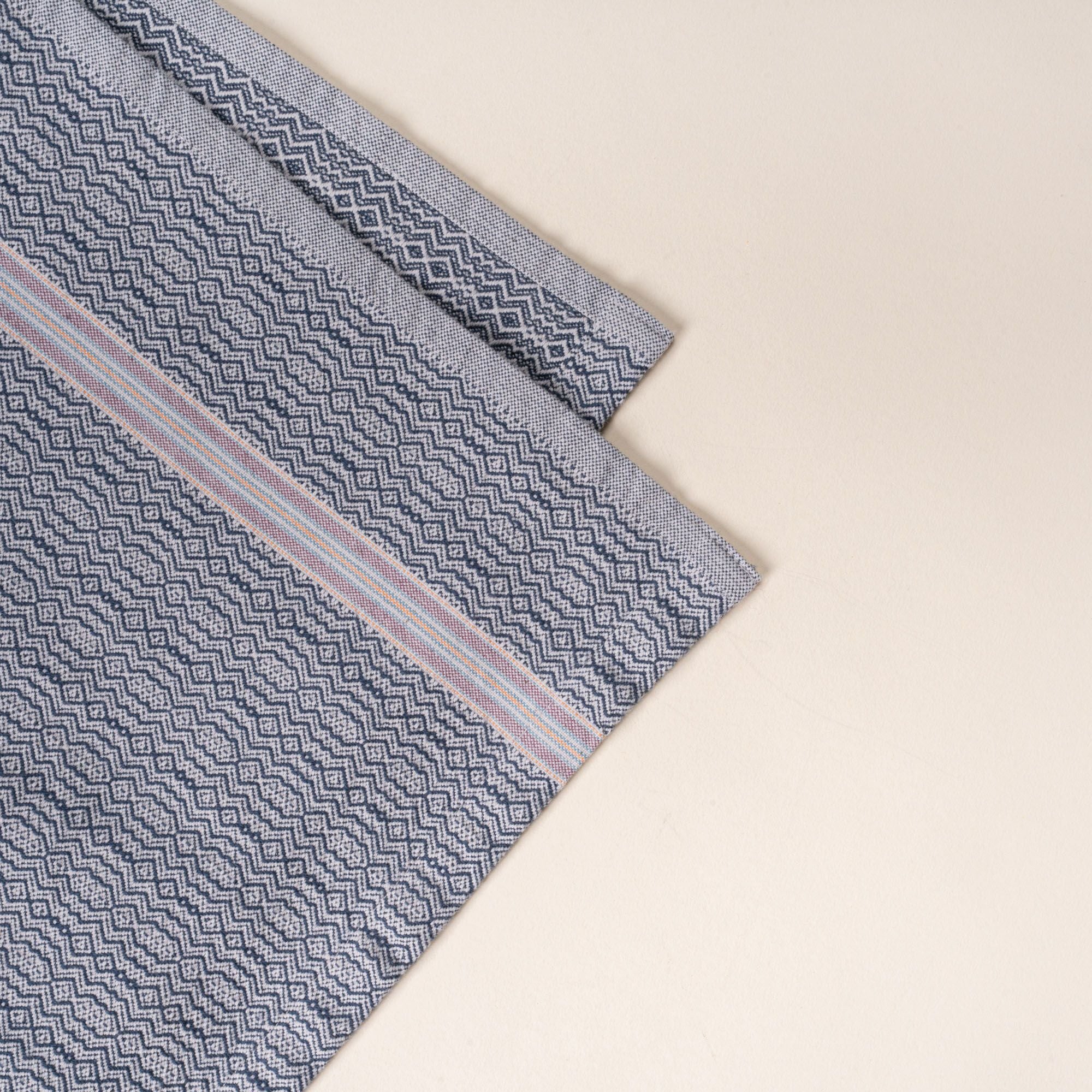 Corner of a grey woven kitchen towel with a subtle textured pattern and slim striped accent, folded neatly on a clean neutral background.